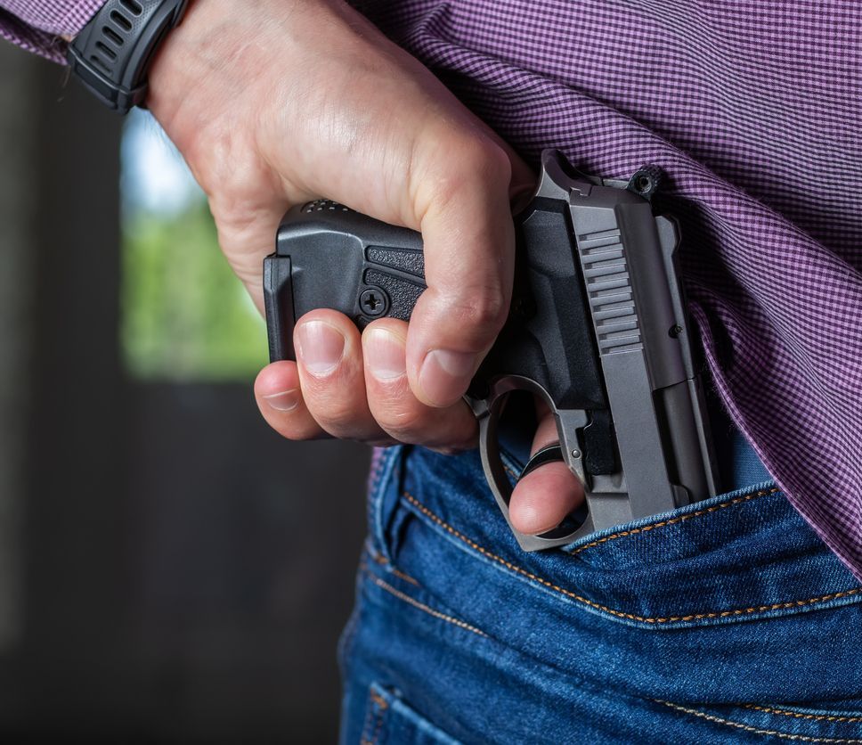 A man holding a gun in his hand behind his back, close-up view. Concepts: crime, attempted murder, a gunshot wound